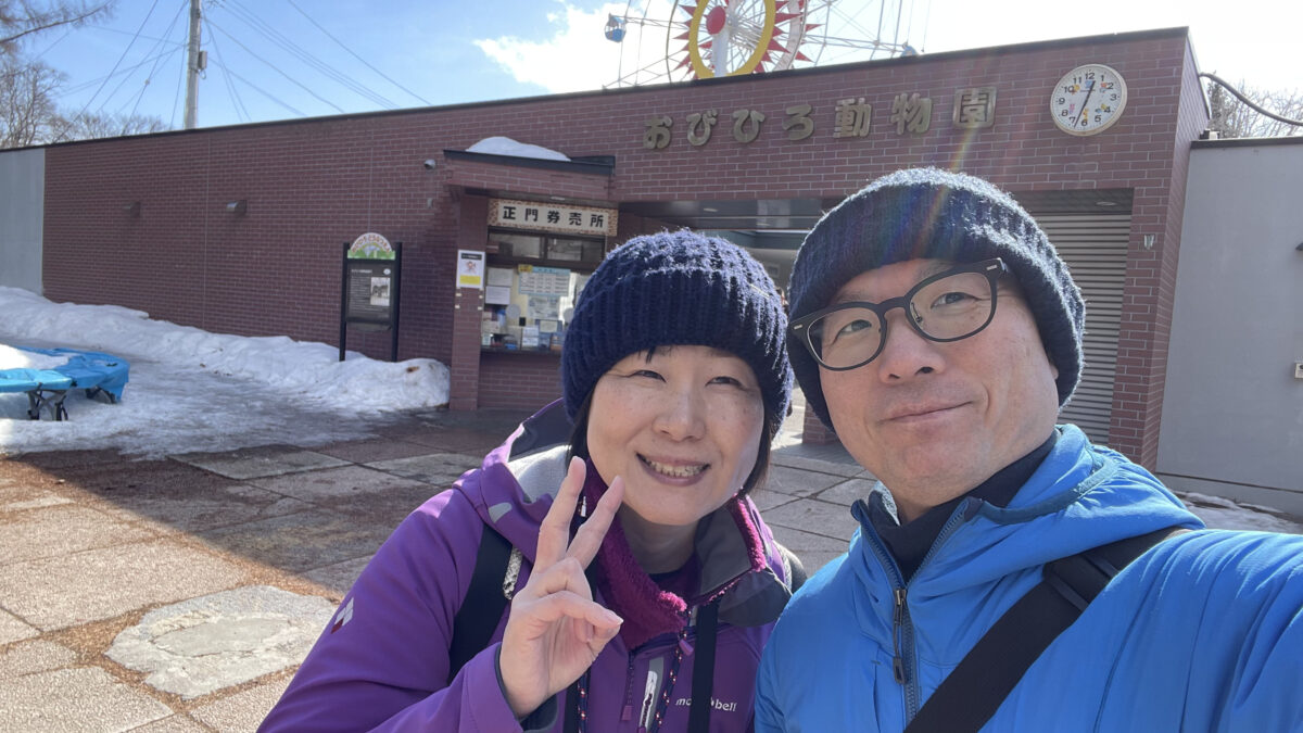 雪の残るおびひろ動物園の正門前で記念撮影をする夫婦