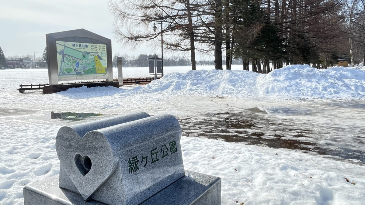 雪に囲まれた緑ヶ丘公園の石製案内標識と広場